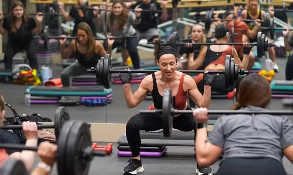 Group of people squatting with barbell over their shoulders.