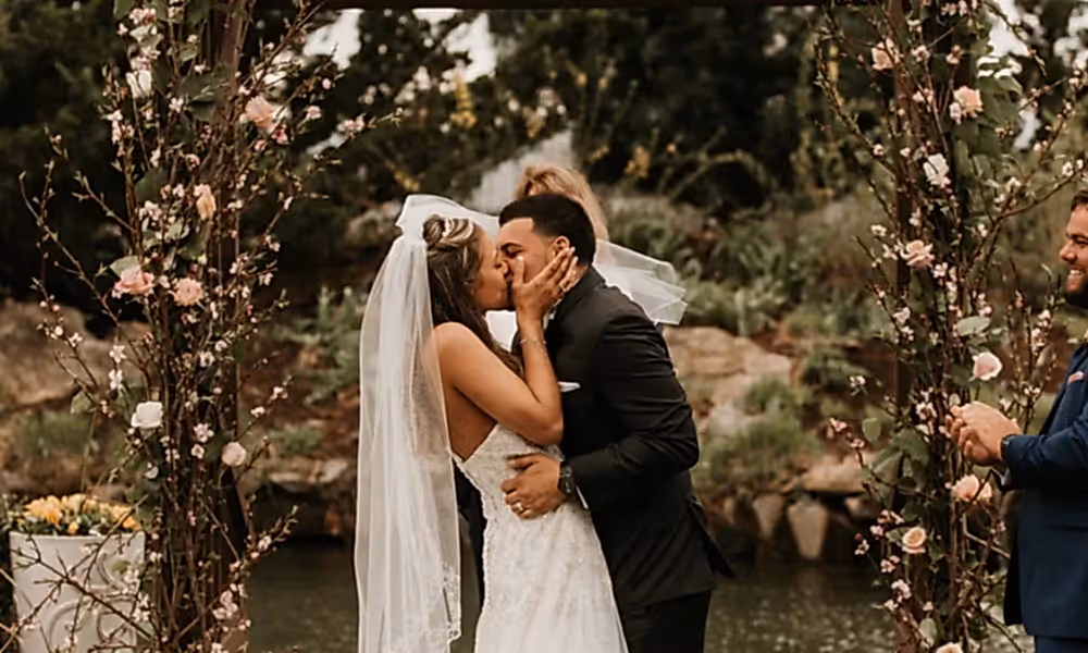 Bride and groom kiss under arch during their Bride walking down the aisle at Wedding Garden ceremony space at Crystal Springs Country Club. 
