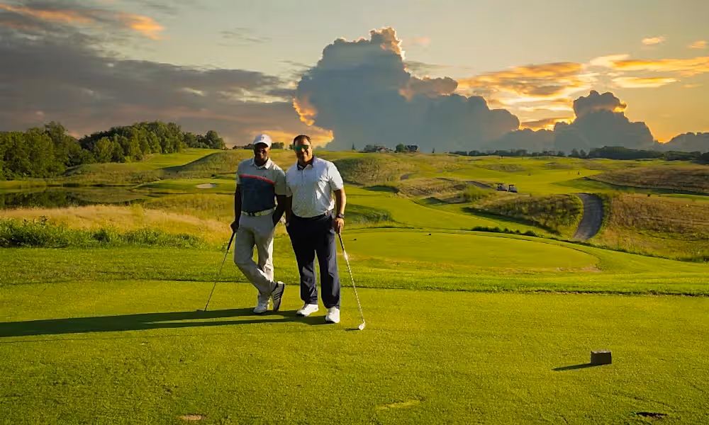 Two golfers stand on Ballyowen Golf Course with sunset behind them. 