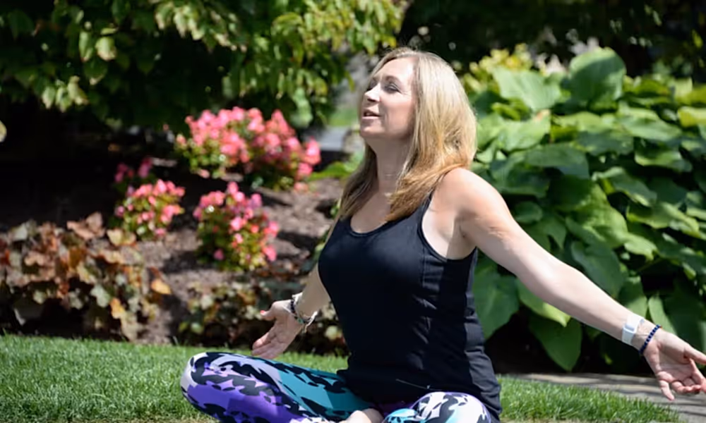 Woman sitting outside doing yoga with her arms stretched out wide