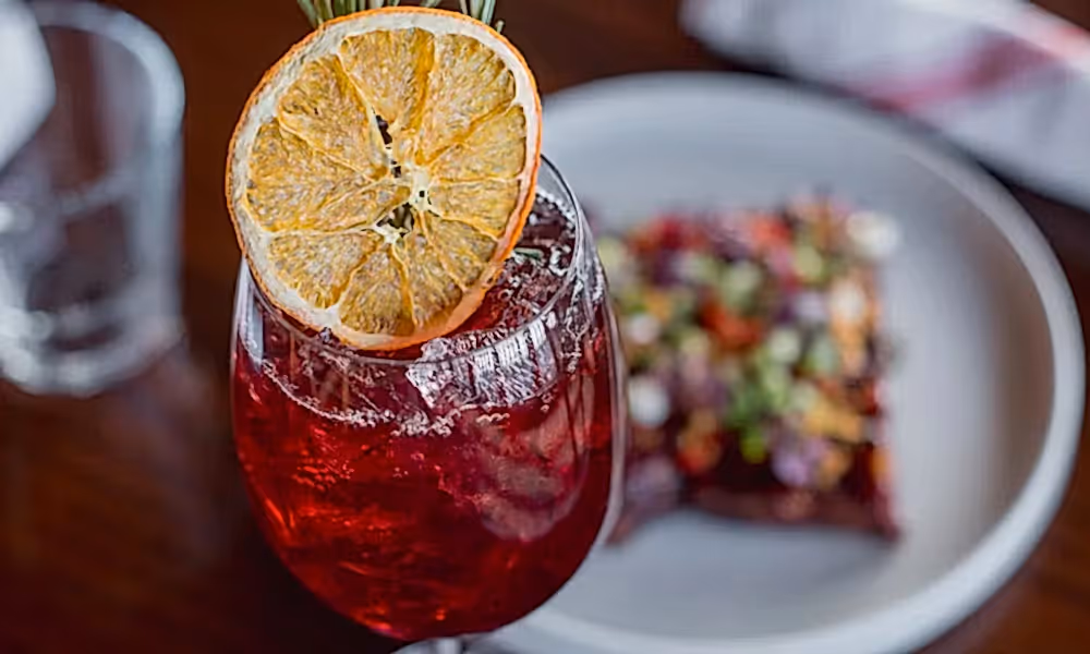 Cocktail topped with rosemary and orange slice.