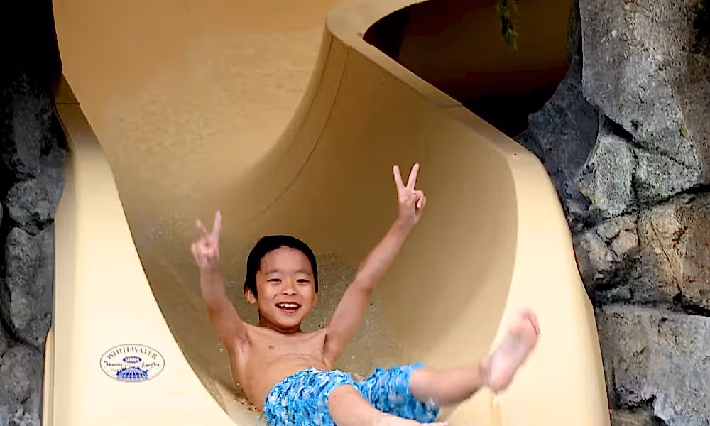 Children showing peace signs on his hands as he slides down Biosphere indoor slide.