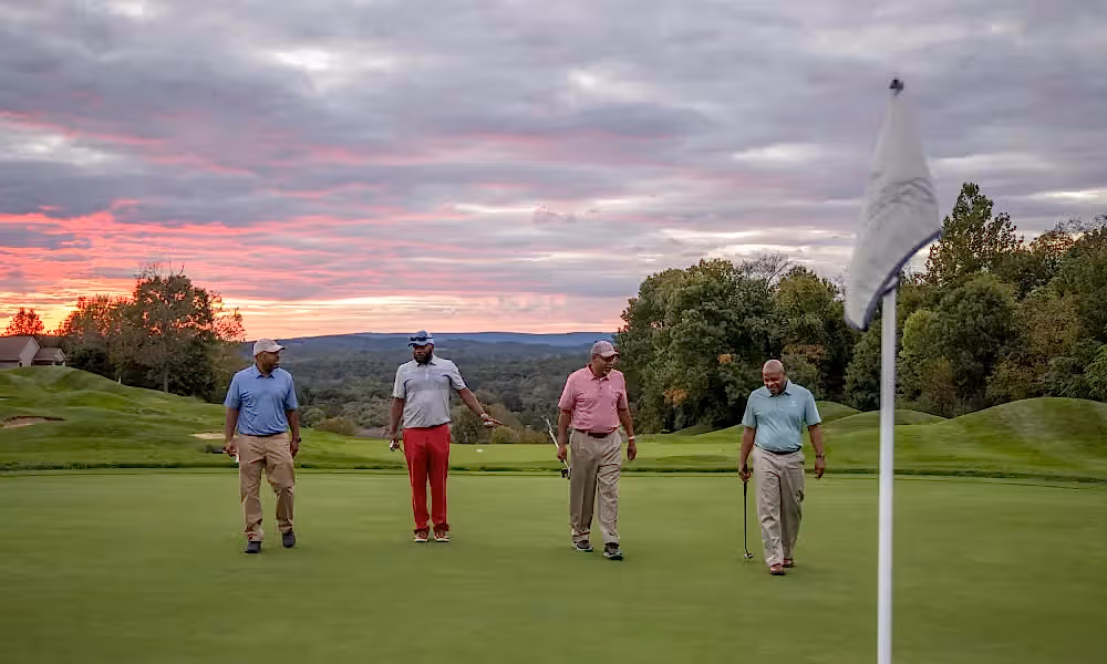 Guys foursome walking on a golf course with the sunset in the background