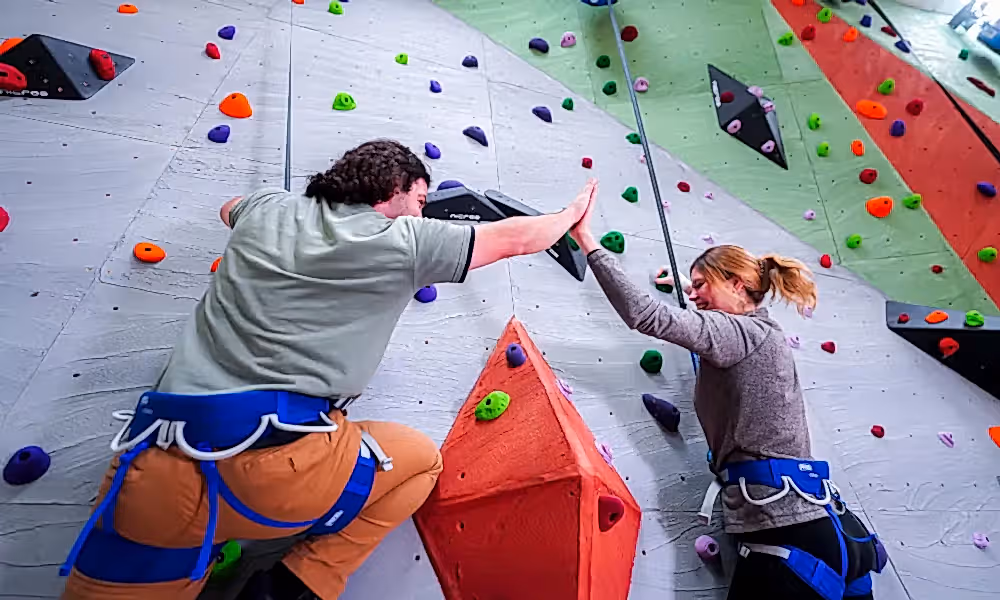 Adults high fiving on rock climbing wall.