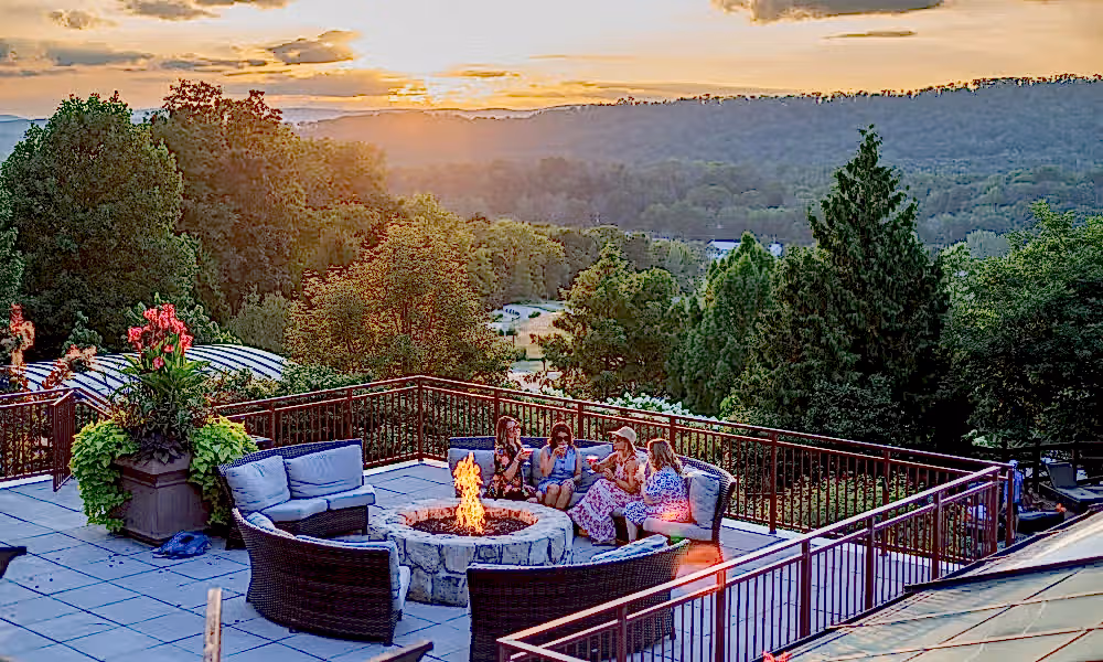 Group of four girlfriends sitting around firepit on Fire &amp; Water terrace overlooking sunset mountain views.